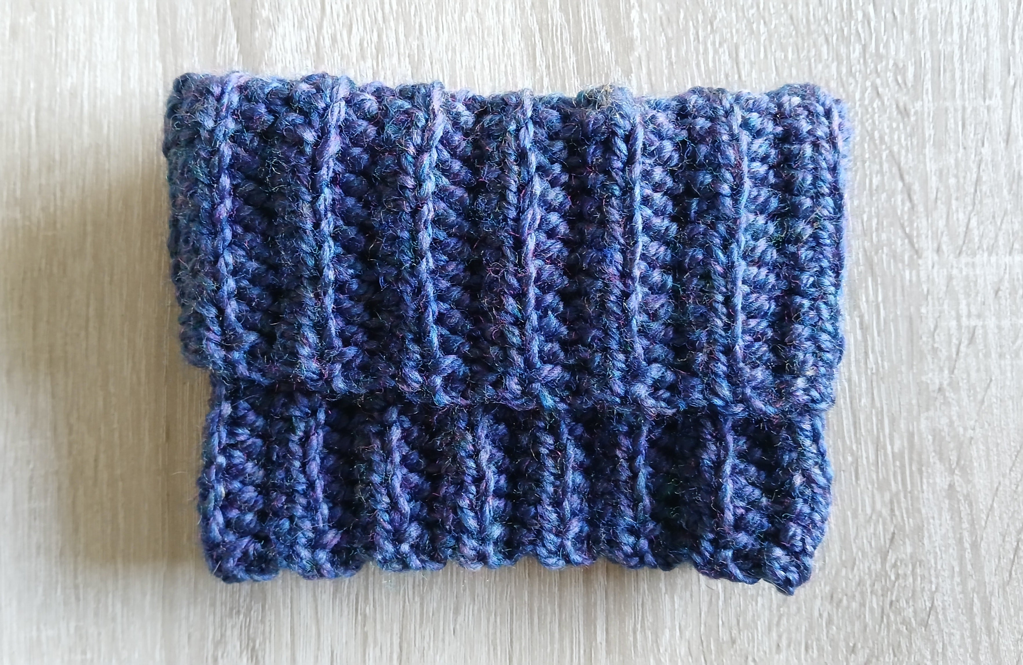 A blue crochet dog snood rolled up like a turtle neck, laying flat on the table 