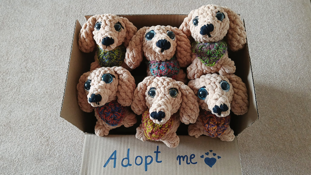 Box of crochet dog toys with 'Adopt me' text on a neutral background
