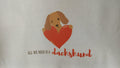 Tote bag with a dachshund holding a heart and text 'All we need is a dachshund' on a beige background.