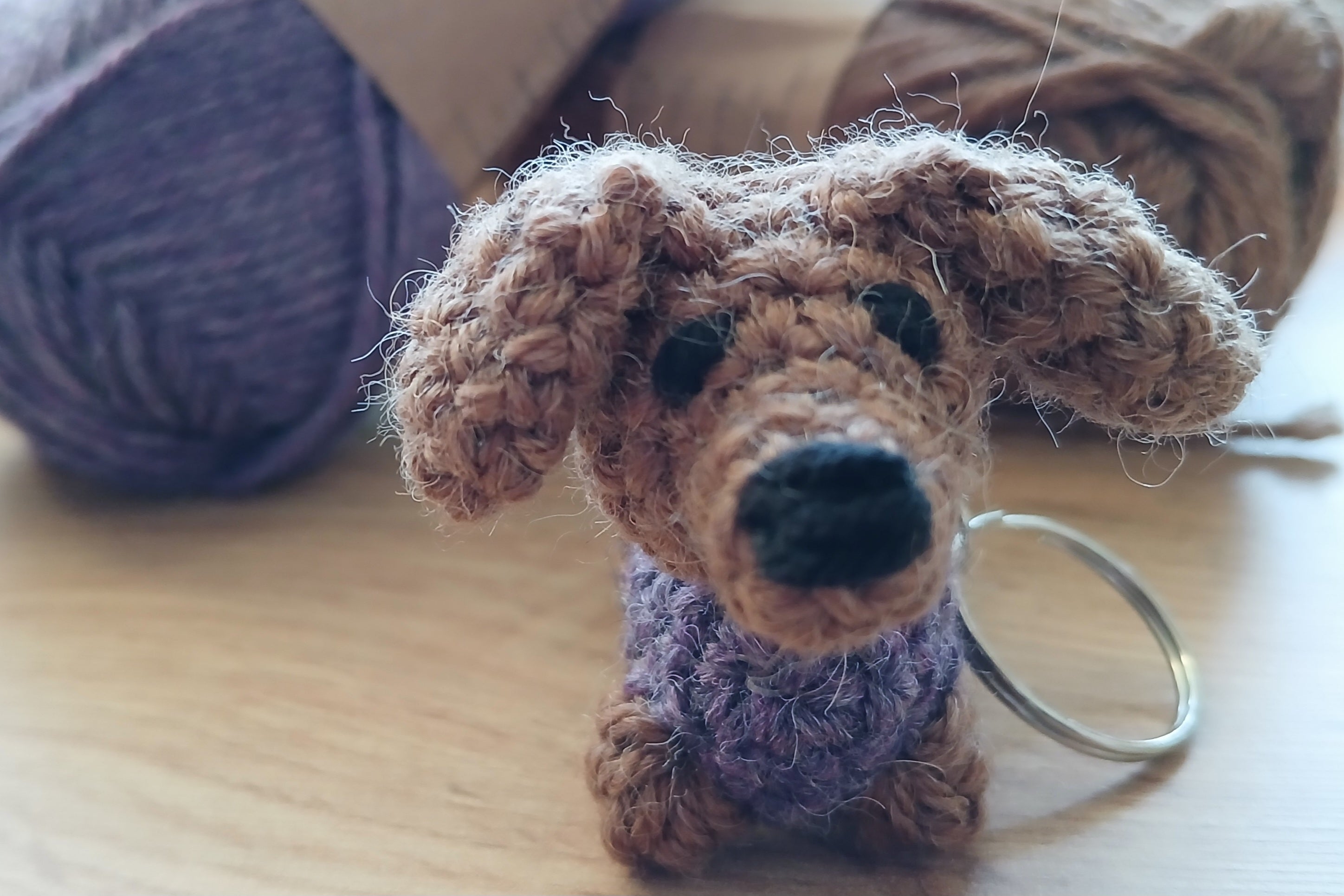 Crochet dachshund keychain with a purple sweater on a wooden surface