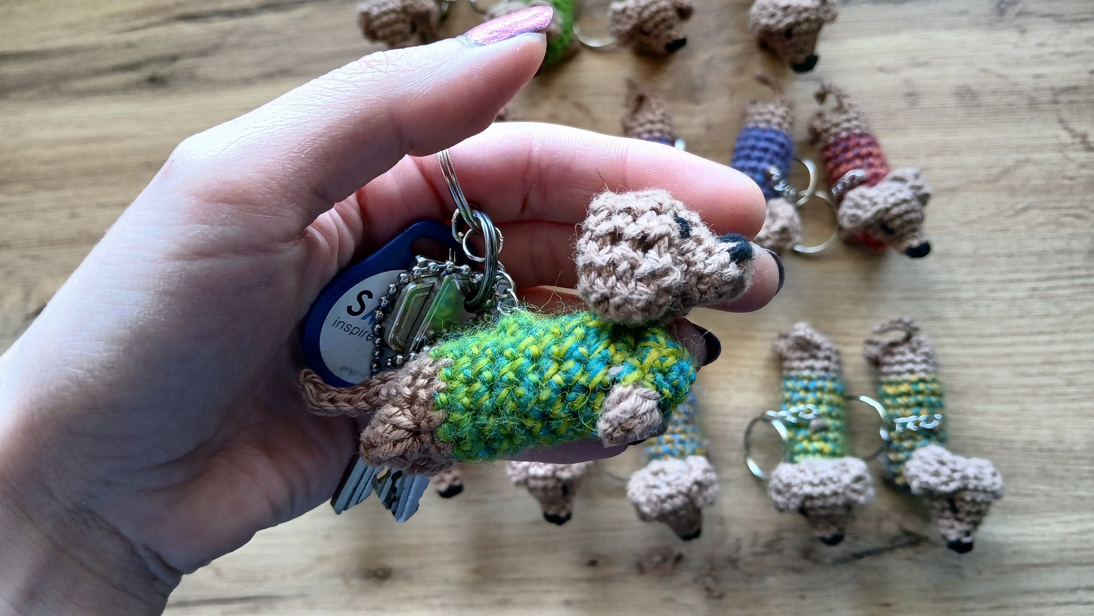 A hand holding a dachshund wearing a sweater keychain to show scale. Keychain fits into woman's palm