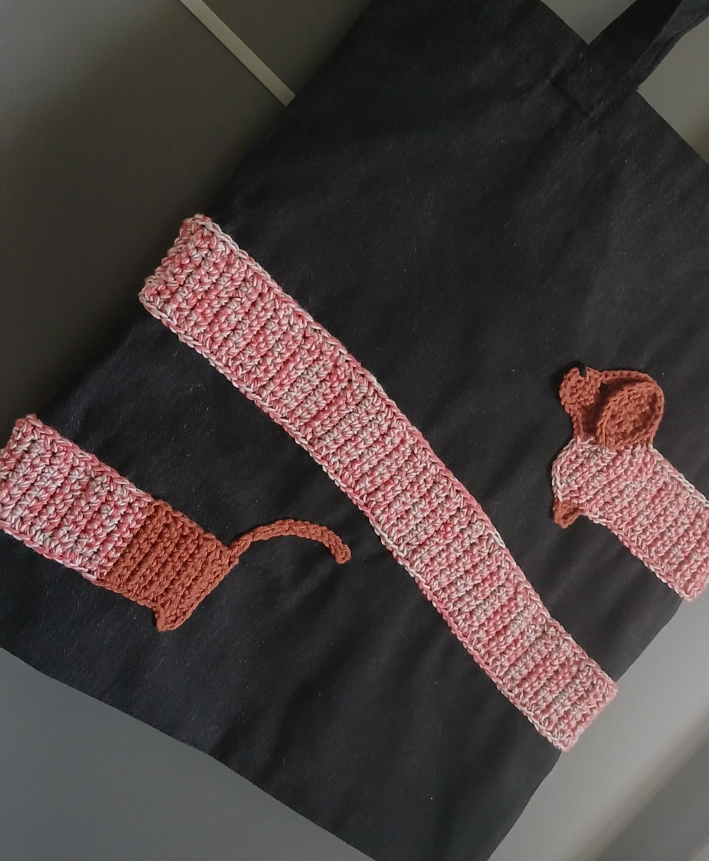 A black cotton tote bag with a dachshund applique wrapped around the bag.