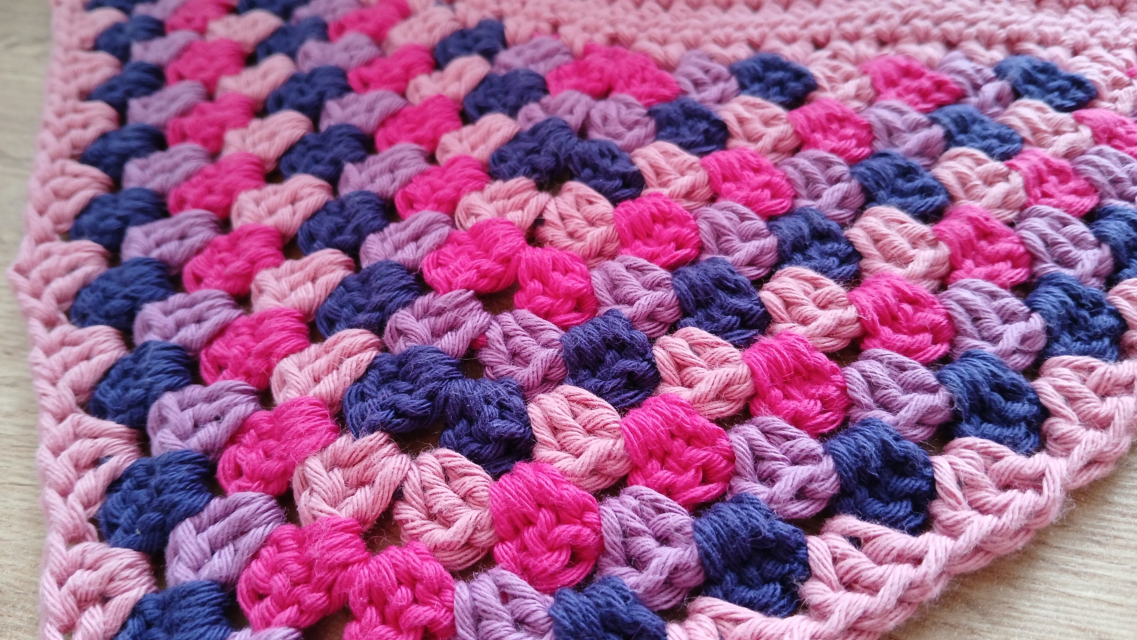 Crocheted dog bandana in pink and blue on a wooden surface