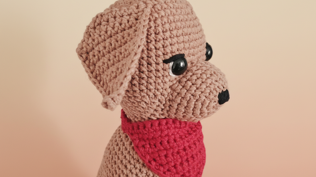 Crocheted dog plushie with a red bandana on a beige background