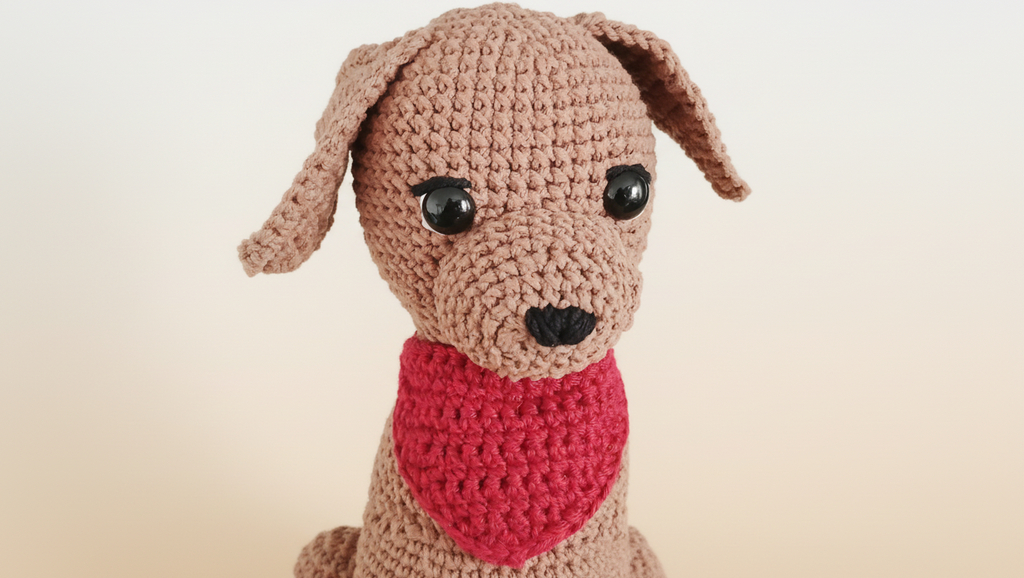 Crocheted Labrador plushie with a red bandana on a beige background
