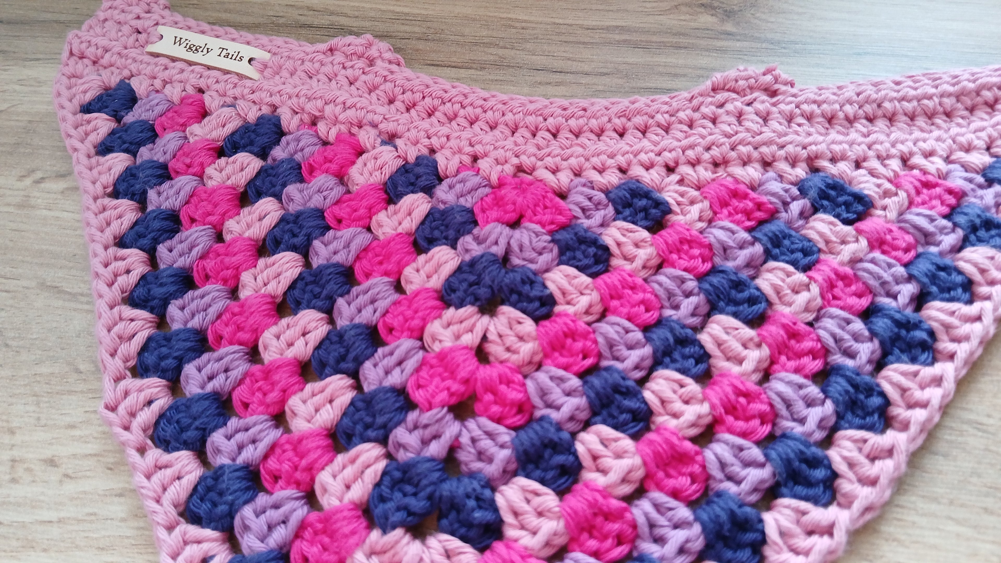 Pink and blue crocheted slip on dog bandana on a wooden surface