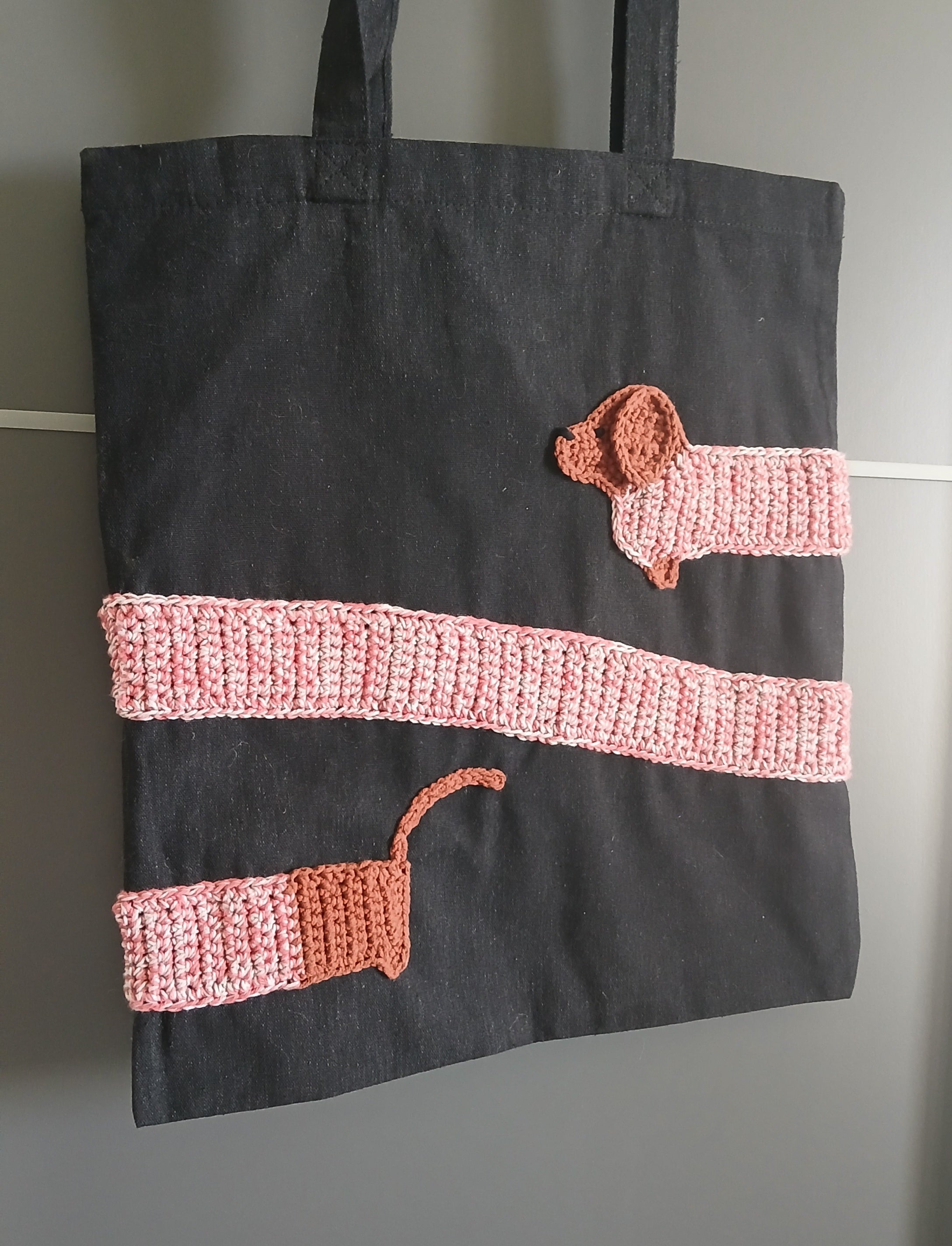 A black cotton canvas bag with a sausage dog applique wrapped around it