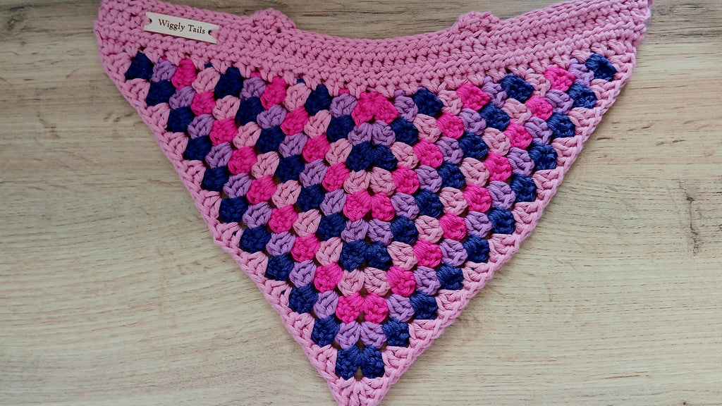 Crocheted triangular shawl with pink and blue pattern on a wooden surface