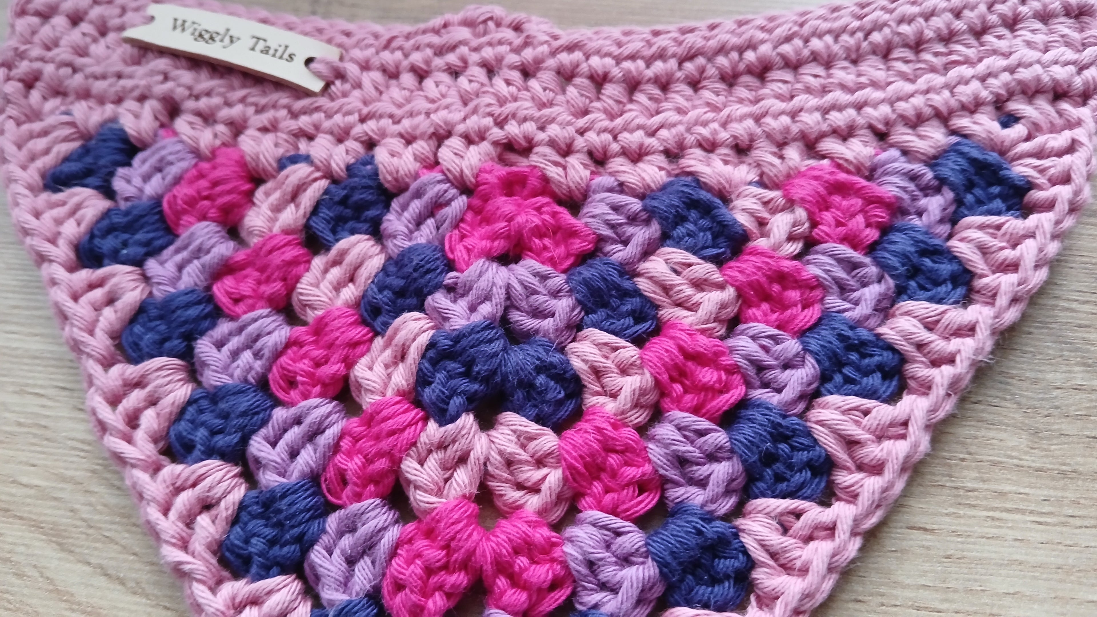 Crocheted pink and blue dog bandana on a light wooden surface