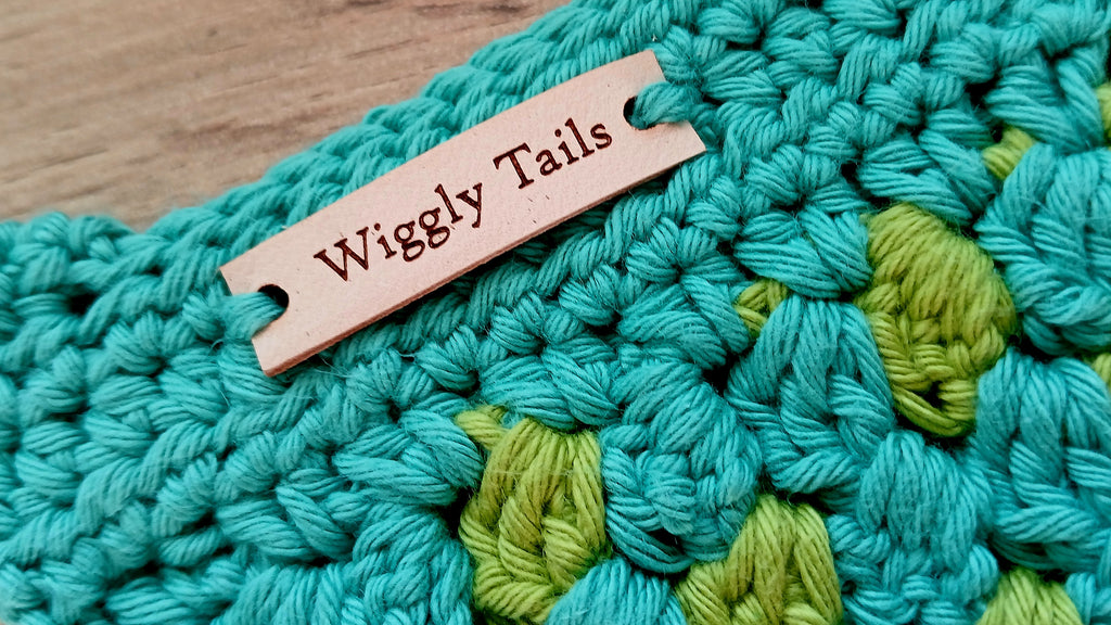 Crocheted teal and green dog bandana with label 'Wiggly Tails'