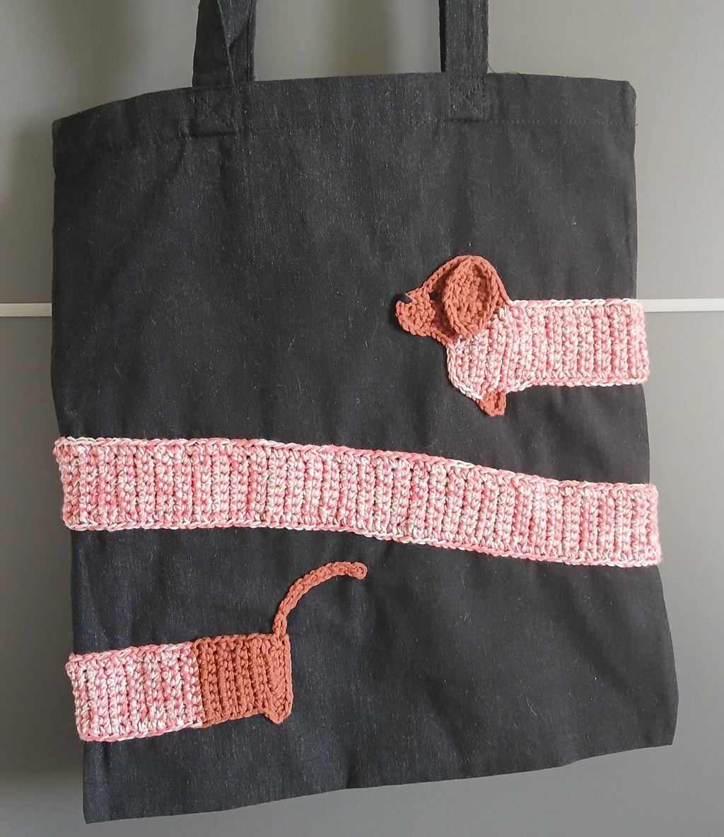 A front of a black tote bag with unique dachshund applique 